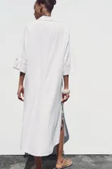 Vestido camisero largo color verde claro, confeccionado en lino. Tiene cuello solapa, escote en V, manga tres cuartos con trabilla y botón, bolsillos delanteros de plastrón, aberturas laterales en el ruedo y cierre frontal con botones.