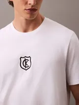 Remera blanca de algodón con cuello redondo y manga corta. Presenta un logo bordado de CK Shield en el pecho.