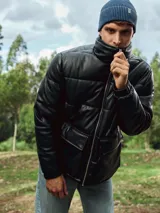 Campera puffer negra de cuero sintético con cuello alto, cierre frontal con cremallera, bolsillos delanteros con solapa y puños elásticos.
