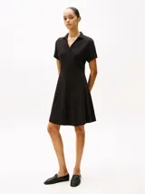 Vestido corto negro de corte evasé, con cuello tipo chomba y mangas cortas.