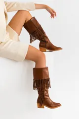 Bota tejana de caña alta color negro, confeccionada 100% en cuero vacuno. Presenta taco de madera foliado en cuero, cierre YKK del lado interior y flecos colocados a mano en la caña.