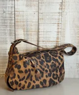 Bolso de hombro color blanco con textura craquelada, correa regulable con hebilla, interior forrado y cierre superior. Incluye llavero y bolsillos internos.