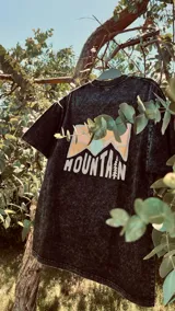 Remera negra con efecto gastado, corte holgado y estampa en la espalda con montañas y la palabra "Mountain" en blanco.