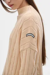 Sweater tejido color borgoña con cuello alto, corte oversize y mangas largas con detalle de trenzas verticales.