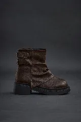 Botas cortas de cuero sintético color marrón oscuro, estilo motociclista o biker, con caña arrugada y hebillas ajustables en el lateral. Suela de goma negra gruesa y dentada.