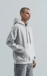 Hoodie gris claro, de corte oversize, confeccionado en frisa premium. Posee capucha ajustable, bolsillo canguro frontal y puños y cintura elastizados. Los cordones de la capucha son negros con texto repetido.
