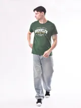 Remera verde con estampa frontal con la inscripción "Brooklyn Varsity Club" en color blanco y detalles en amarillo.