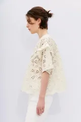 Blusa color crudo con bordado calado tipo broderie, de corte holgado, escote redondo, manga corta con volados en la sisa y detalle de alforzas en el canesú.