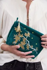 Bolso de mano tipo clutch, color verde esmeralda, de terciopelo con bordado de flores amarillas y blancas. Incluye un cierre superior y un colgante de borla dorada.