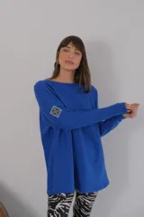 Buzo azul de viscosa con cuello redondo y manga larga. Presenta un aplique con diseño geométrico en el brazo izquierdo.
