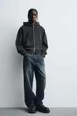 Mocasín negro con flecos. Parte superior lisa con efecto desgastado. Detalle de antifaz y flecos con puntas metálicas en el empeine. Horma cuadrada. Suela con volumen.