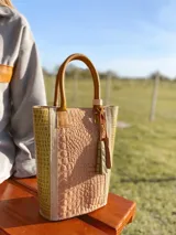 Bolso matero de cuero color nude con textura croco y laterales en color pistacho. Tiene manijas cortas de cuero color suela y un dije de cuero con flecos.