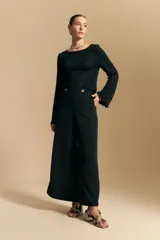 Top negro de manga larga acampanada con escote pronunciado en la espalda que se ajusta con lazos. La tela presenta una textura sutil con brillo, similar a un animal print discreto.