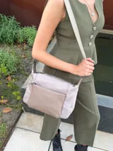 Bandolera de diseño moderno, color beige rosado, con correa regulable y bolsillo frontal con cierre.