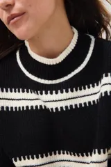 Sweater negro de punto con detalles en blanco, diseño de rayas y cuello redondo.