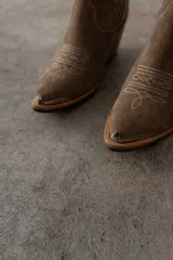 Bota corta de gamuza color marrón oscuro, con puntera cuadrada y detalles de costuras decorativas. Tiene un taco de madera con forma cónica.