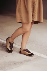 Zapatillas urbanas de cuero color beige con puntera y cordones marrones. Presentan un panel de animal print en el talón y suela de goma color caramelo.