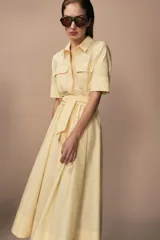 Vestido midi camisero color ladrillo, confeccionado en popelina de algodón. Presenta cuello solapa, manga corta con puños abotonados, bolsillos laterales ocultos y bolsillos de parche con solapa en el pecho. Incluye cinturón lazada en el mismo tejido y cierre frontal con botones ocultos.