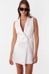 Minivestido blanco tipo blazer sin mangas, con cuello solapa, doble botonadura cruzada, bolsillos ojal y tira de ajuste en la espalda.