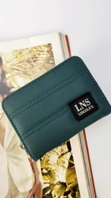 Billetera corta de tela capitoneada color verde oscuro, con cierre alrededor y tapa. Incluye varias reparticiones con tarjeteros y bolsillos internos. Correa de mano desmontable.