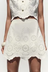 Falda pantalón corta de tiro alto color blanco con bordados florales perforados y forro interior. Cierre lateral con cremallera oculta.