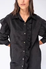 Camisa larga negra de poliéster con textura de pana fina, con mangas largas y cierre frontal con botones. Presenta volados verticales en el frente.