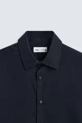 Camisa negra de manga larga con cuello italiano y cierre frontal de botonadura. Presenta un tejido con estructura de fácil cuidado.