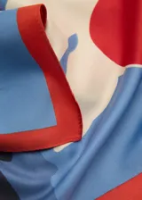 Pañuelo cuadrado de tela satinada con estampado de flores rojas y blancas sobre fondo celeste. Tiene un borde liso color rojo.