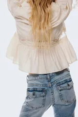 Jeans de denim azul claro con efecto lavado y desgaste sutil. Tienen un corte ajustado hasta la rodilla y luego se abren en un estilo acampanado (flare). Son de tiro bajo y presentan bolsillos delanteros abiertos y bolsillos traseros con solapa y botón.