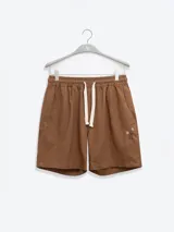 Bermuda de lino color marrón con bordado de flores blancas en la pierna izquierda. Tiene cintura elástica con cordón de ajuste, bolsillos laterales y un bolsillo trasero tipo parche.