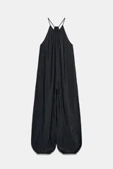 Mono largo negro de tejido ligero y arrugado, con escote halter y tirantes finos. El corte es muy holgado en el torso y las piernas terminan en puños elásticos ajustados.