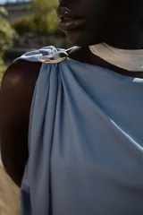 Top celeste de satén con cuello amplio, manga asimétrica y fornitura dorada en el hombro.