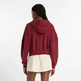 Campera con capucha y cierre frontal, color rojo oscuro/bordó, de corte cropped y calce holgado. Presenta el logo New Balance bordado en el pecho.
