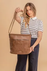 Cartera tipo bandolera de tamaño mediano confeccionada en símil cuero color marrón. Presenta una correa larga regulable, dos compartimientos principales y un bolsillo frontal con cierre de cremallera.
