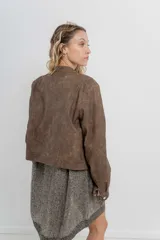 Chaqueta tipo biker de cuero ecológico (PU) color marrón con acabado desgastado, cuello Mao con broches metálicos, cierre frontal y bolsillos con cremallera.