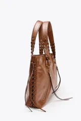 Bolso shopper de hombro color marrón, con flecos y trenzados en el cuerpo. Tiene doble cremallera metálica, asa doble con detalles metálicos y trenzados, y bolsillo interior. Cierre mediante cremallera metálica.