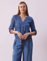 Blusa celeste de tencel, marca Alex & Parker. Cuello a la base, escote en V y abertura central con botones. Delantera con bolsillos. Largo de manga regulable con presilla y botón. Terminación de ruedo con nudo.