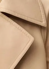 Abrigo color beige con cuello solapa, doble botonadura, cinturón y bolsillos laterales.
