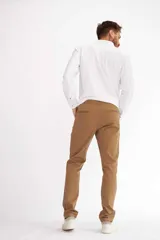 Pantalón de vestir color beige, de corte recto, con bolsillos laterales y traseros. Se ajusta a la cintura con cinturón de cuero marrón.