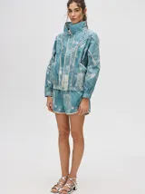 Campera rompevientos estilo biker con capucha desmontable, color celeste con estampado de nubes blancas y detalles en blanco.