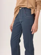 Pantalón de jean recto color azul oscuro, confeccionado en gabardina de algodón gastada, con costuras y atraques en hilo blanco contrastante. Presenta un botón de madera en el cierre frontal.