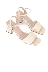 Sandalias de cuero color crema, con punta cuadrada, tira ancha sobre los dedos y pulsera al tobillo con hebilla. El tacón es cuadrado y mide 8 cm.