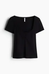 Remera corta negra de punto suave, corte ajustado, con costura fruncida en el centro del busto y escote corazón pronunciado con ribete de picot.