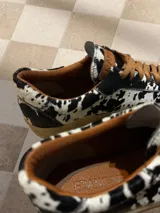 Zapatillas bajas con estampado animal print de vaca en blanco y negro, con cordones marrones y suela color caramelo.