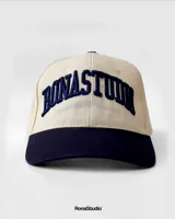 Gorra de béisbol beige con visera y botón superior azul marino. Presenta bordado frontal en azul marino con la inscripción "Bonastun South American League".