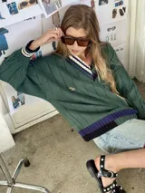 Buzo tejido verde con escote en V, cuello con rayas blancas y azul marino, y puños y ruedo con detalle de rayas.