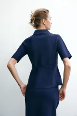 Chaqueta azul marino de punto con cuello solapa y manga corta. Incluye cinturón fino con hebilla dorada y cierre frontal con botones a tono.