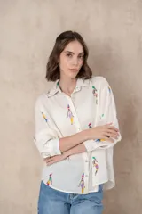 Camisa blanca con bordados coloridos de figuras femeninas, corte clásico y manga larga.