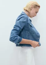 Chaqueta de denim celeste de corte cropped, con cuello camisero, cierre frontal con botones, mangas largas con puños abotonados y dos bolsillos de parche con solapa en el pecho.