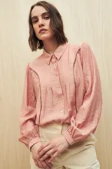 Camisa color salmón con textura rayada, cuello clásico, cierre frontal con botones y mangas largas con puños elásticos. Presenta detalles calados en el frente.